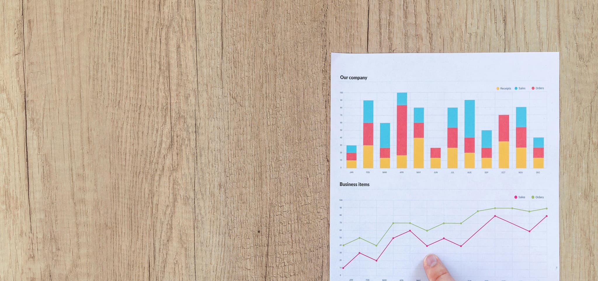 A hand points to a line graph on a wooden table, with a bar chart above labeled 'Our Company,' showing data.