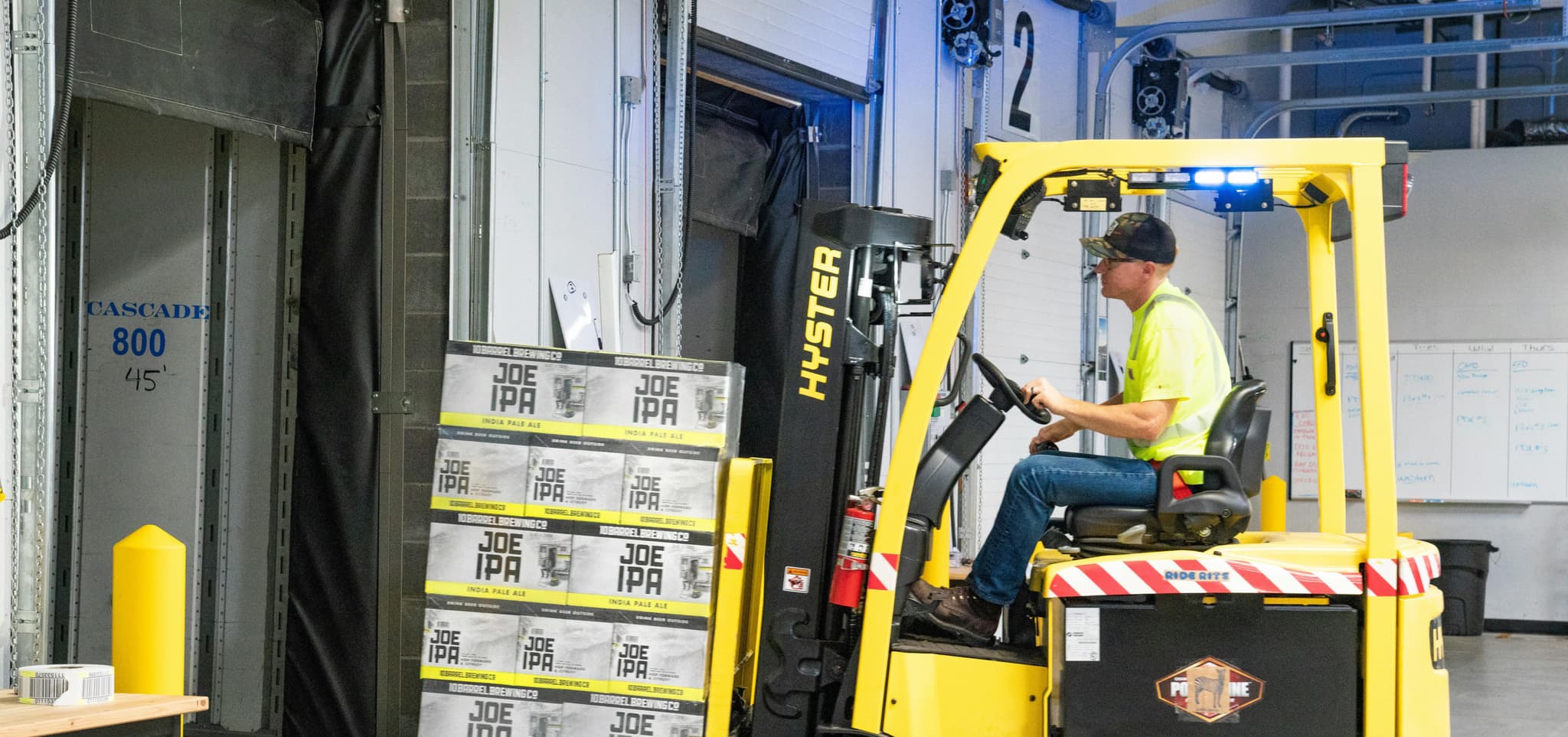 A worker in a safety vest operates a yellow forklift, moving packages into a loading area with focus and efficiency.