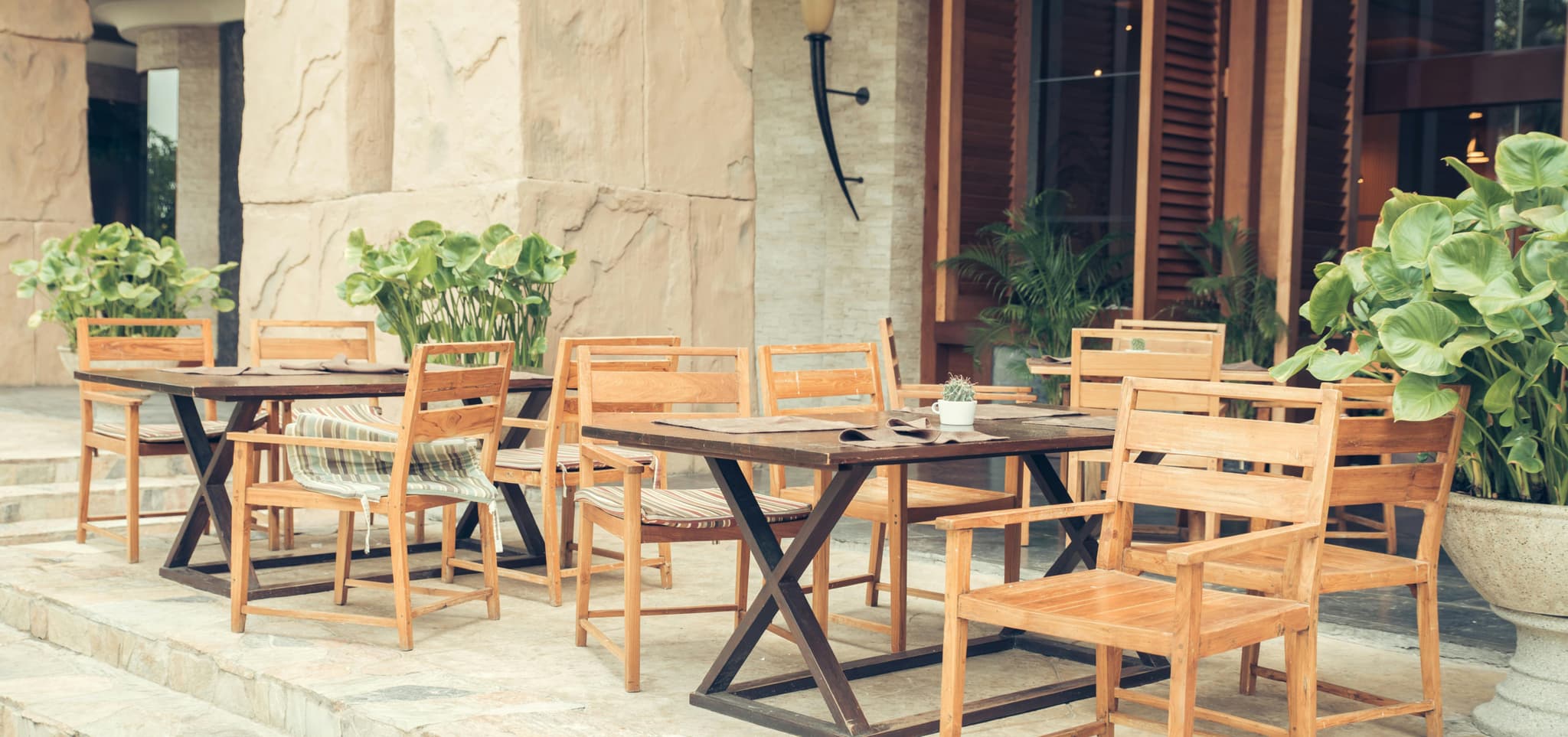 Outdoor café with wooden tables, chairs, and lush potted plants, creating a warm, inviting, and peaceful vibe.