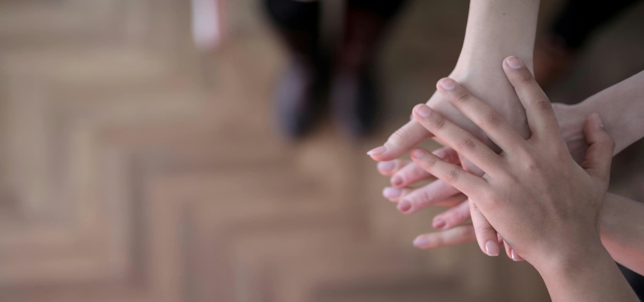 A group of hands stacked together, symbolizing unity and support, with a blurred background highlighting connection.