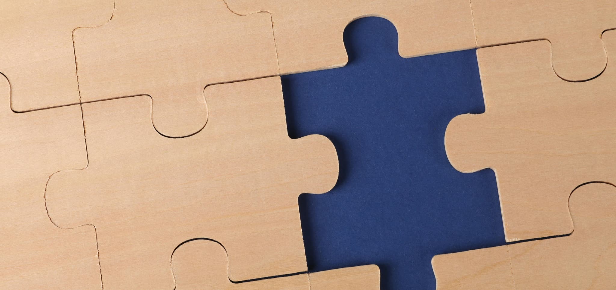 Close-up of wooden puzzle pieces with one missing, revealing a dark blue background, symbolizing unfinished work.