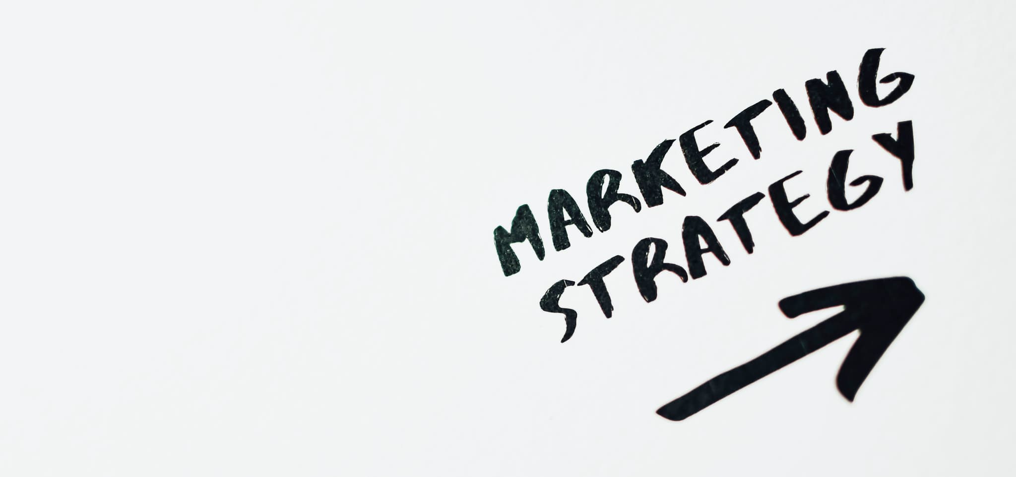 Handwritten 'Marketing Strategy' with an arrow pointing right on a white background.