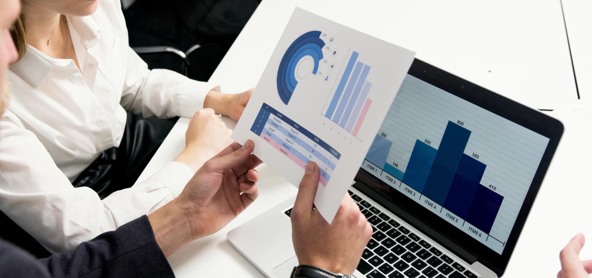 Two people review charts and graphs on paper and a laptop at a table.