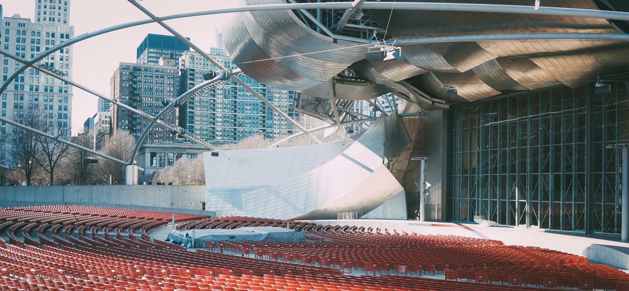 Outdoor amphitheater with red seats and a metallic structure, set against skyscrapers under a clear sky.